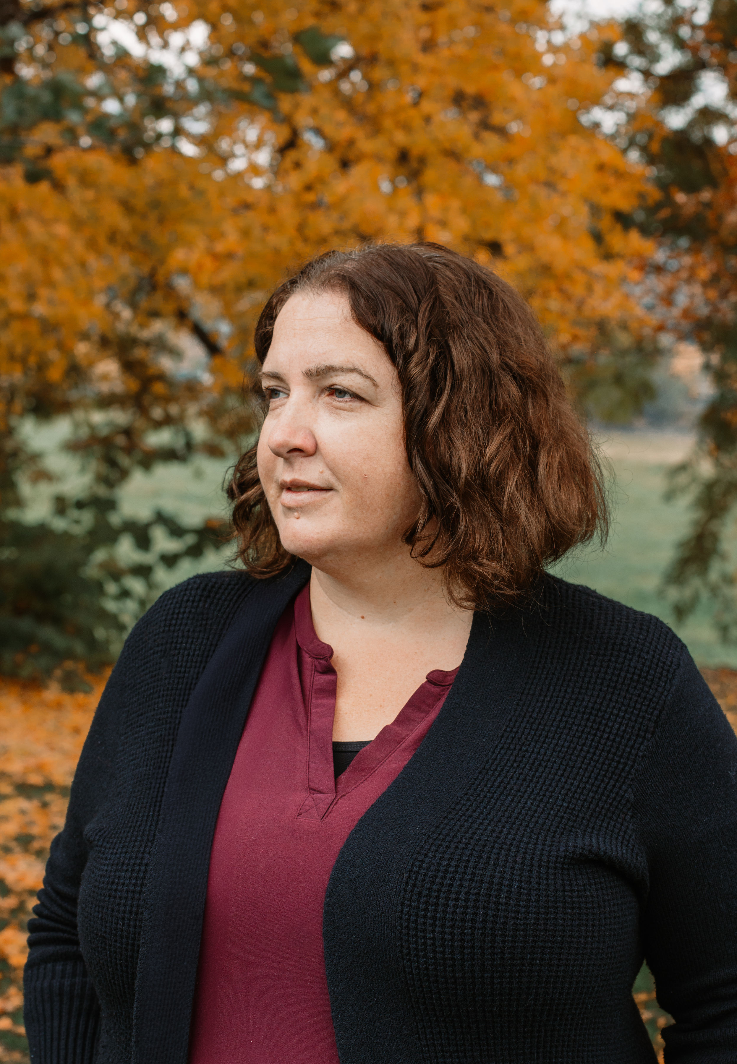 Julie Bond, founder of Peace Mediation, standing among autumn leaves.